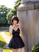 A woman in a black dress standing next to a stone wall.