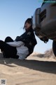 A woman sitting on the ground next to a car.