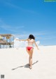 A woman in a red bikini walking on a sandy beach.