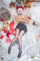 A woman laying on top of a pile of snow next to a Christmas tree.