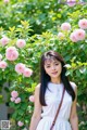 A woman standing in front of a bush of pink flowers.